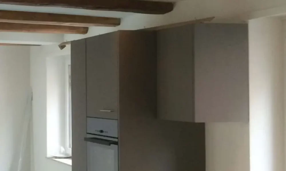 Trockenbau-Referenzprojekt: Präzise beplankte Deckenfelder zwischen historischen Holzbalken mit integrierten LED-Spots. Glatt verspachtelte Wände (Q3-Qualität) und vorbereiteter moderner Küchenbereich bei einem Wohnungsumbau.